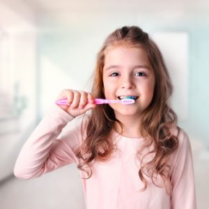 girl in pink shirt brushing her teeth with toothbrush