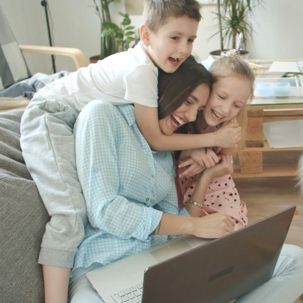 female middle age playing wth kids on couch with grey laptop on lap